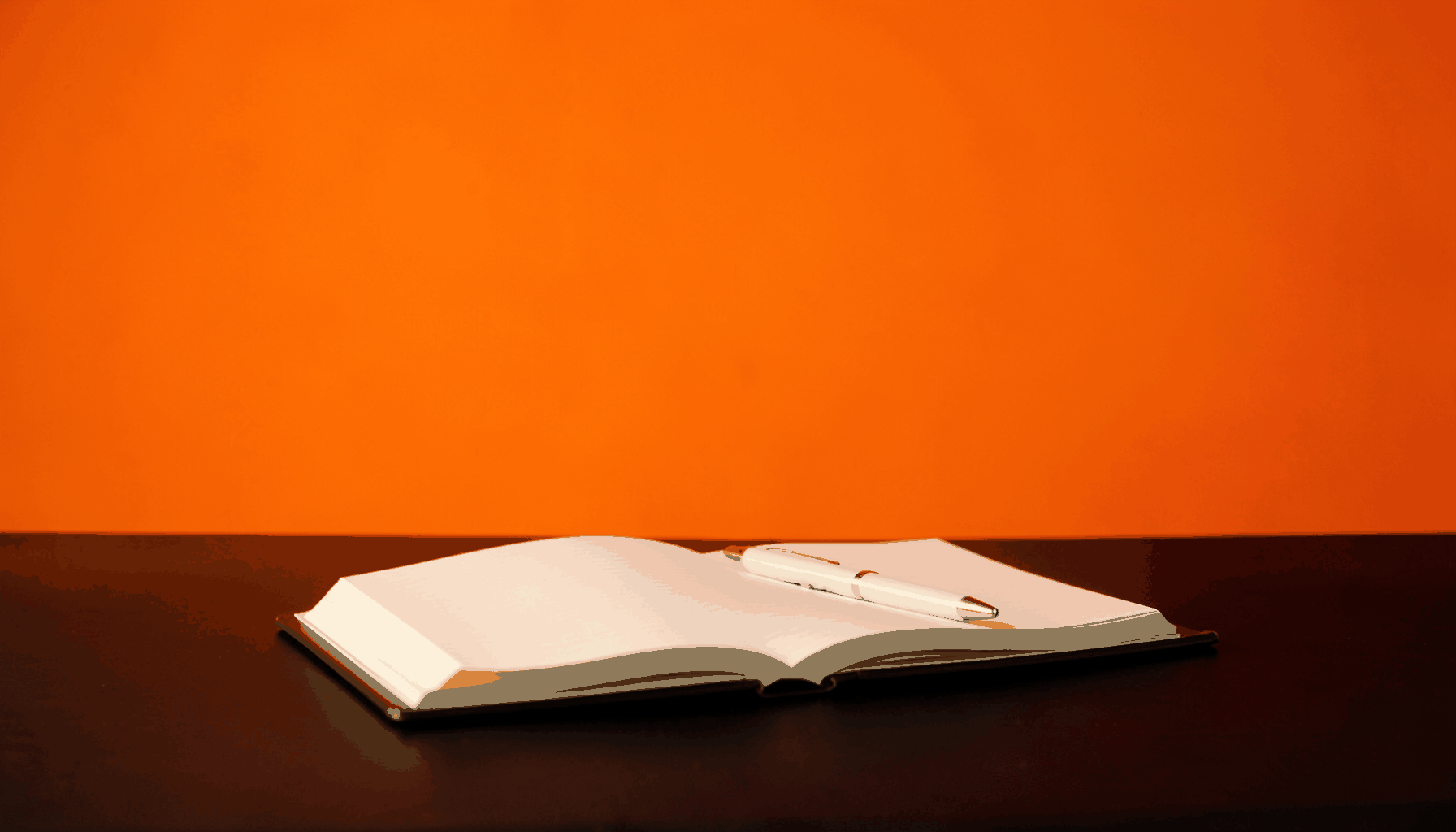 A simple open notebook and pen resting on a dark table, warm amber light from one side, quiet and minimal