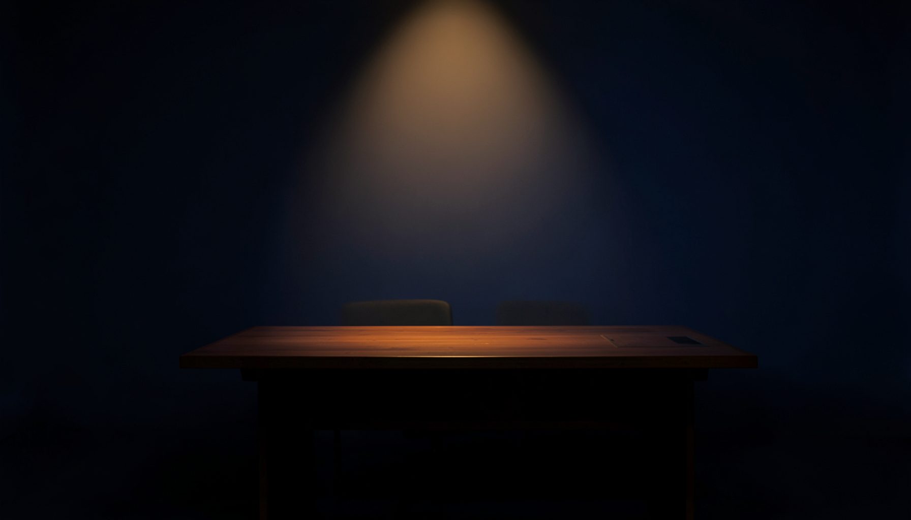 Dark charcoal studio backdrop with a single warm amber spotlight, evoking a quiet newsroom desk at night